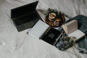A cozy flat lay of a laptop, journals, and snacks on a bed for a relaxed work-from-home setup.