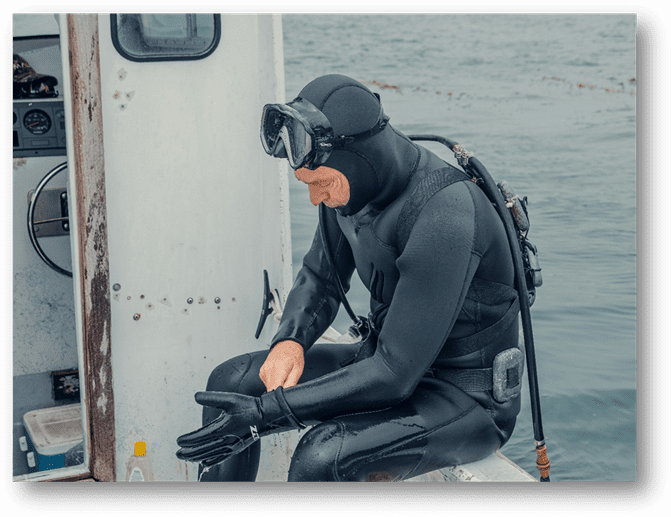 A diver sitting on a boat and putting on gloves, preparing for the dive.